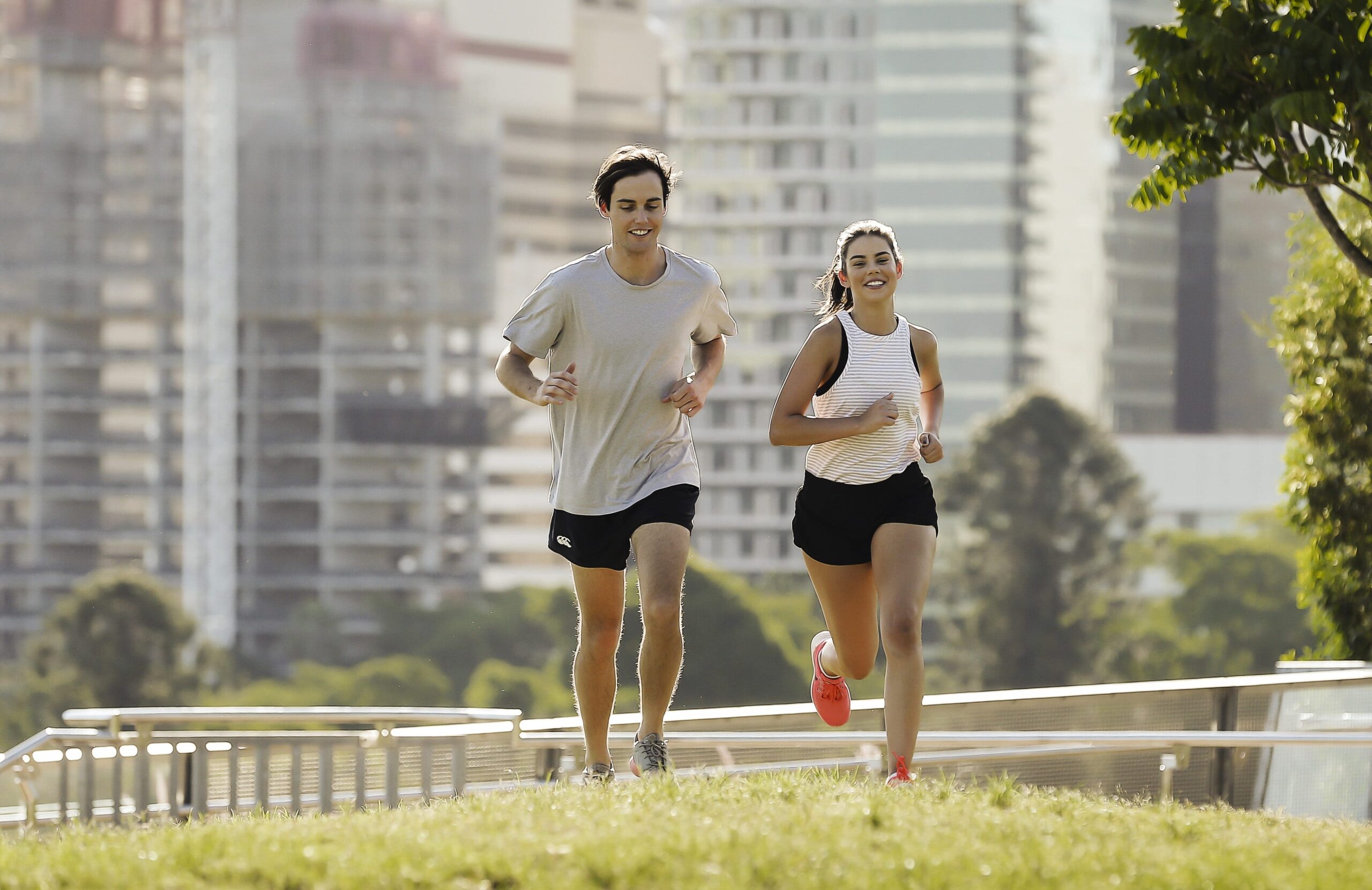 male and female running on grass with city in background